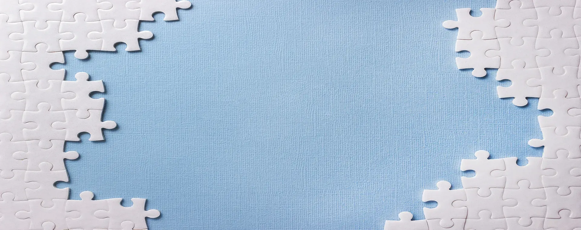 A partly assembled white jigsaw puzzle with a large gap of blue backing board showing through the middle.